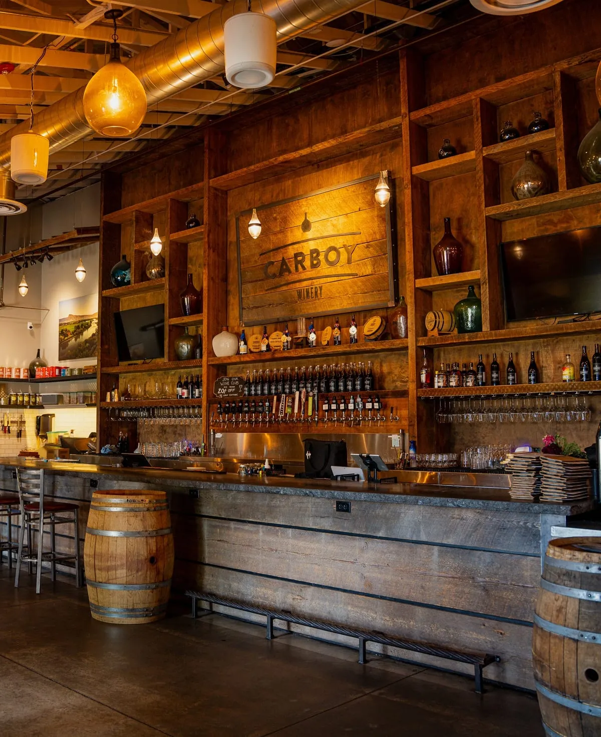 Inside Carboy Winery, Littleton — the CARBOY sign on the reclaimed-wood wall above the barrel-lined bar