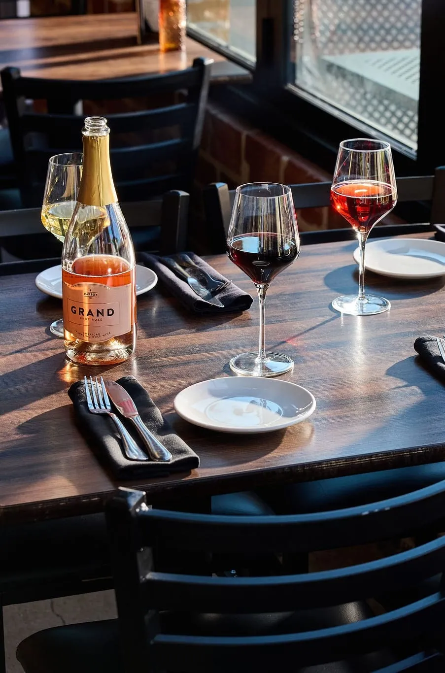 Carboy wine on the table — a bottle of Carboy GRAND rosé and glasses of wine by the tasting-room window